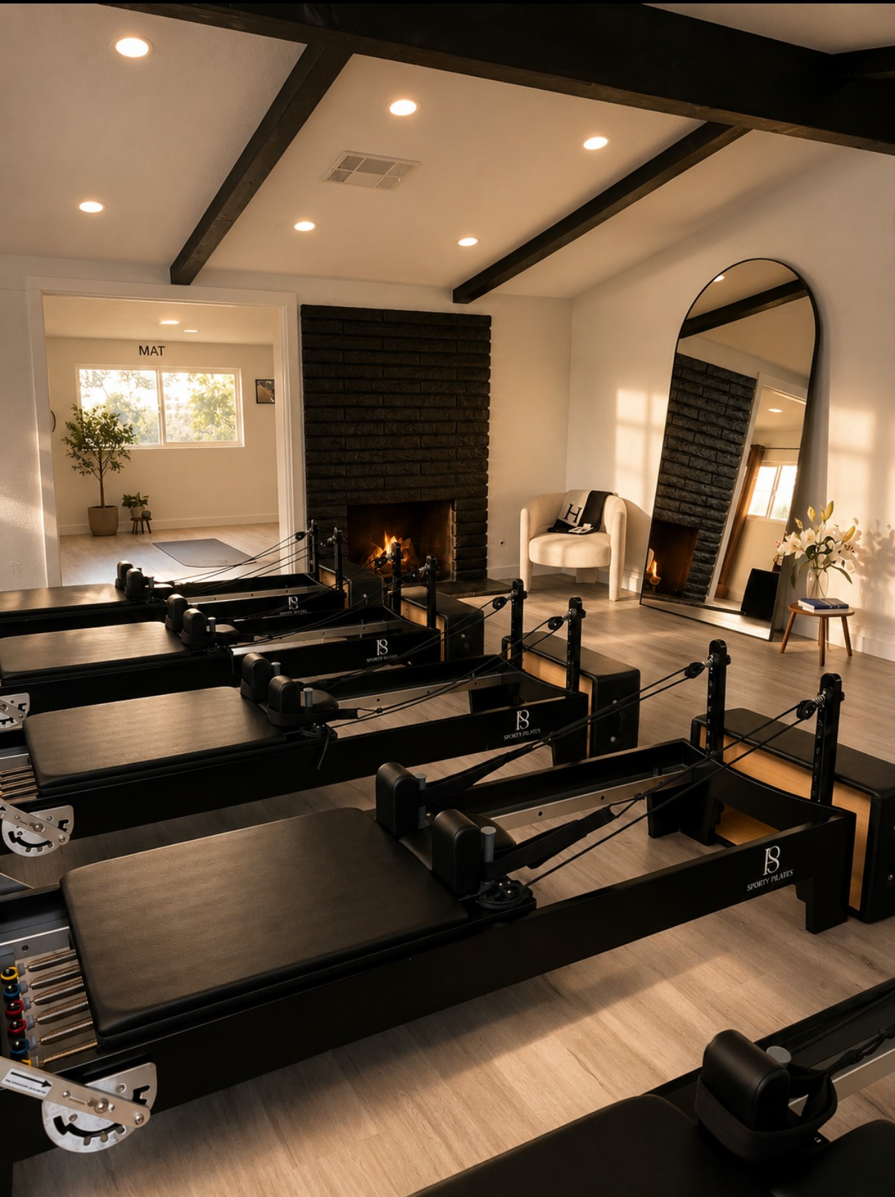 Black reformers arranged in the Sporty Pilates home studio beside a fireplace and arched mirror.